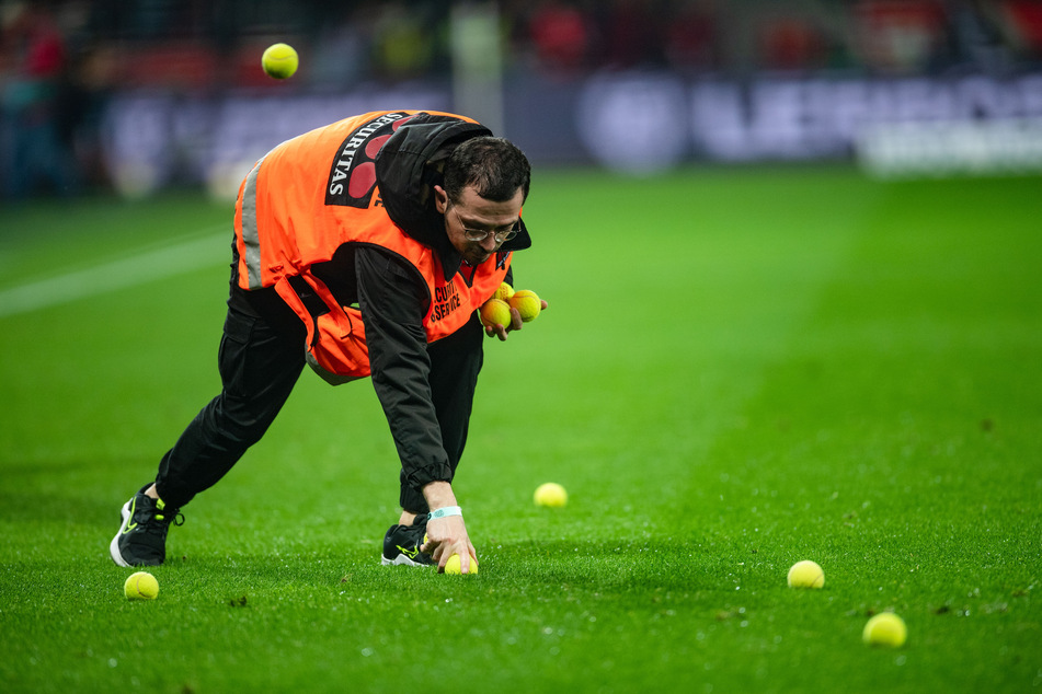 Ein Ordner sammelt Tennisbälle auf, die Kölner Fans auf den Rasen geworfen haben.