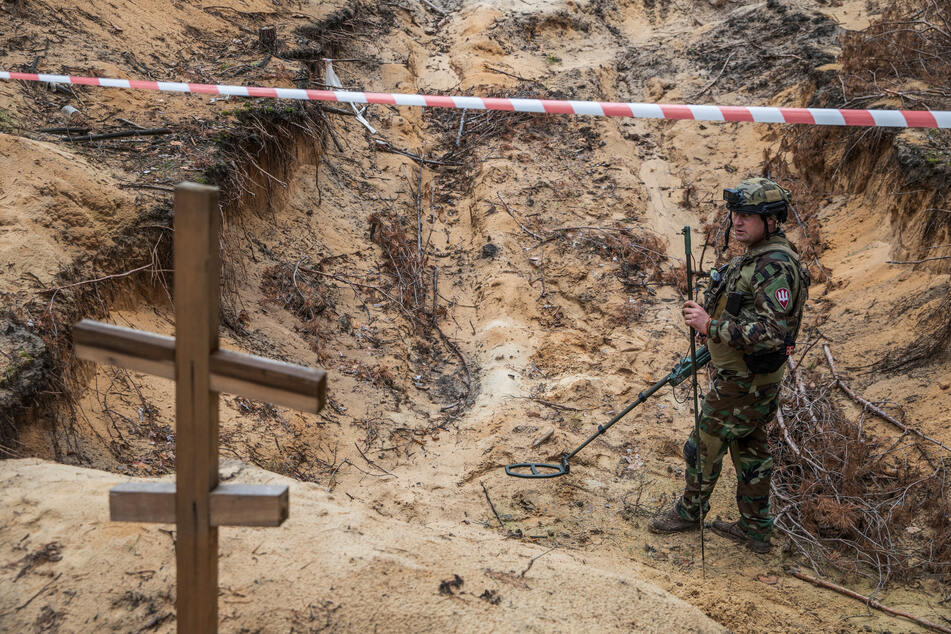 A Ukrainian serviceman uses a metal detector to inspect one of the mass graves discovered.