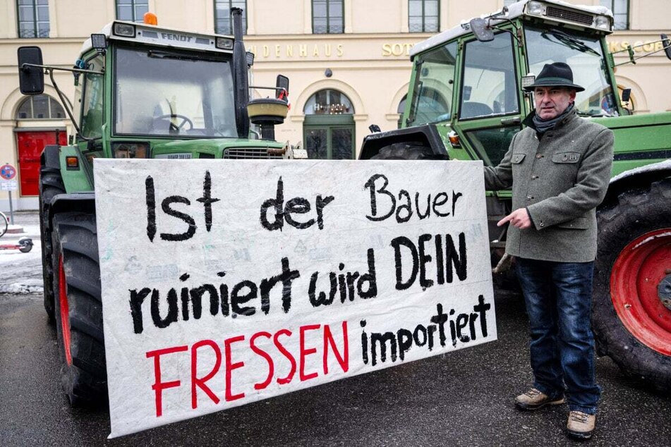 Hubert Aiwanger (52, Freie Wähler), stellvertretender Ministerpräsident, steht während der Demonstration in München vor einem Traktor, an dem ein Schild mit der Aufschrift "Ist der Bauer ruiniert, wird Dein Fressen importiert" hängt.