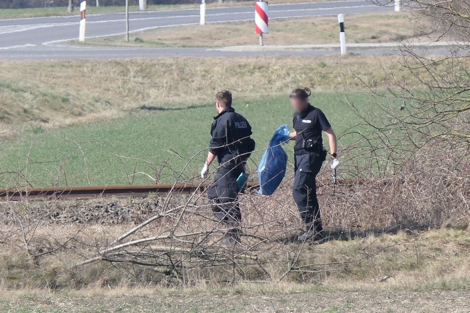 Eine Polizistin trägt einen blauen Sack in Richtung Auto.