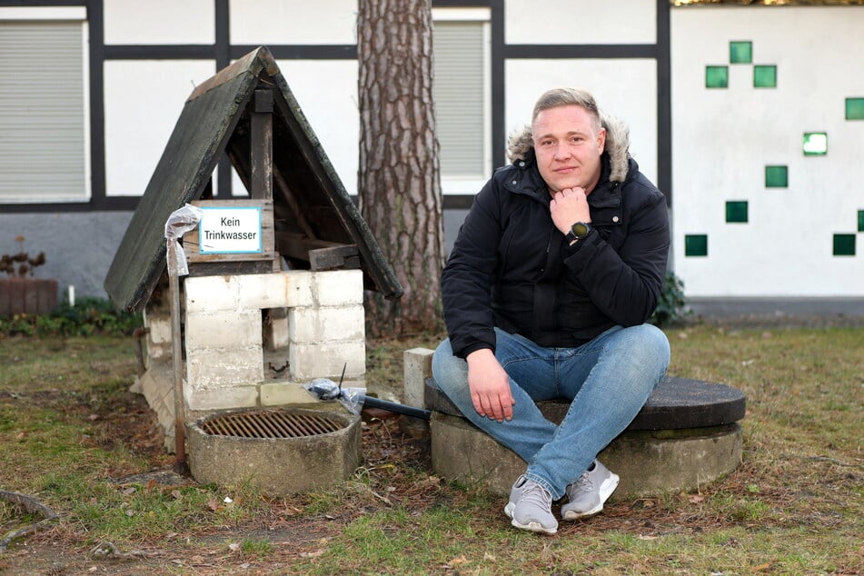 Vereinschef und Ortschaftsbeirat Steven Grünberg (38) sitzt vor einem stillgelegten Brunnen am Waldbad in Weixdorf.