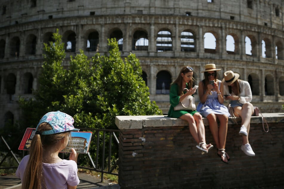 Eine Gruppe junger Frauen sitzt vor Kolosseum. In Italien hat der späte Beginn der Tourismussaison den Neustart des Urlaubssektors nach der Lockerung von Corona-Beschränkungen gebremst.