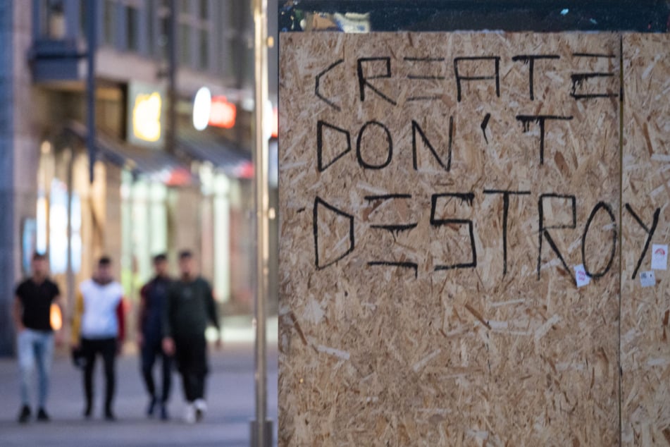 Die Worte "Create don't Destroy" (dt: "Erschaffe statt zu zerstören") stehen auf Holzplatten, mit denen eine beschädigte Scheibe einer Werbetafel abgedeckt ist.