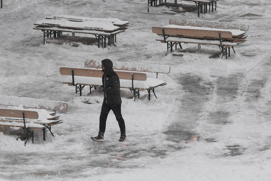 Ein Mann geht über die verschneite Terrasse der Bergstation am Osterfelderkopf im Wettersteingebirge nach einem Temperatursturz.
