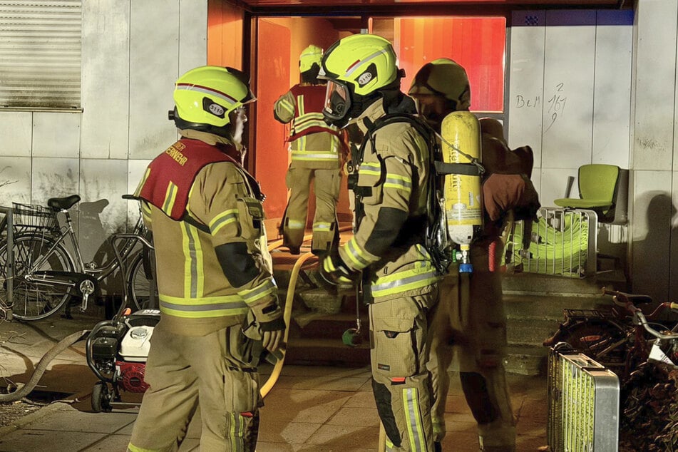 Bei einer Lagebesprechung bereiten sich Feuerwehrkräfte mit Atemschutz und Sauerstoffflaschen auf den Einsatz im Keller des Hauses vor.