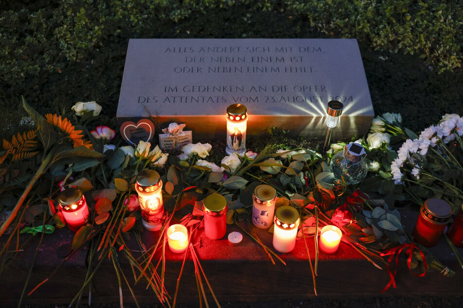 Blumen und Kerzen befinden sich am Gedenkstein unweit des Tatorts für die Opfer des Terroranschlags von Solingen am ersten Jahrestag. (Archivbild)