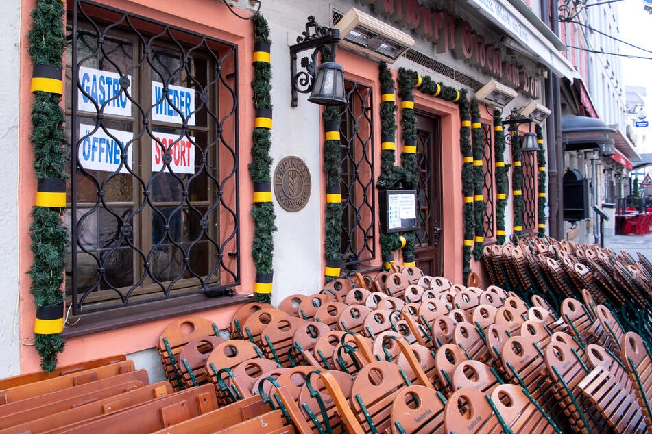 Tische und Stühle stehen vor einem Restaurant. Im Fenster hängen Zettel mit der Aufschrift "Gastro wieder öffnen - sofort".