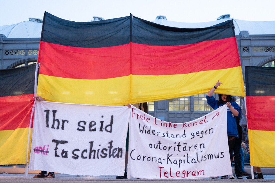 Die Teilnehmerin des Protests steht hinter einer Deutschland-Flagge und hält Spruchbänder hoch.