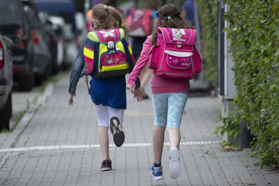 Zwei Schülerinnen einer Grundschule rennen in Frankfurt am Main mit einem Schulranzen auf dem Rücken die letzten Meter bis zum Schulhof.
