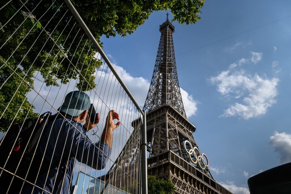 A tourist tries to snap photos behind fences of the 2024 Paris Olympic rings on the Eiffel Tower.