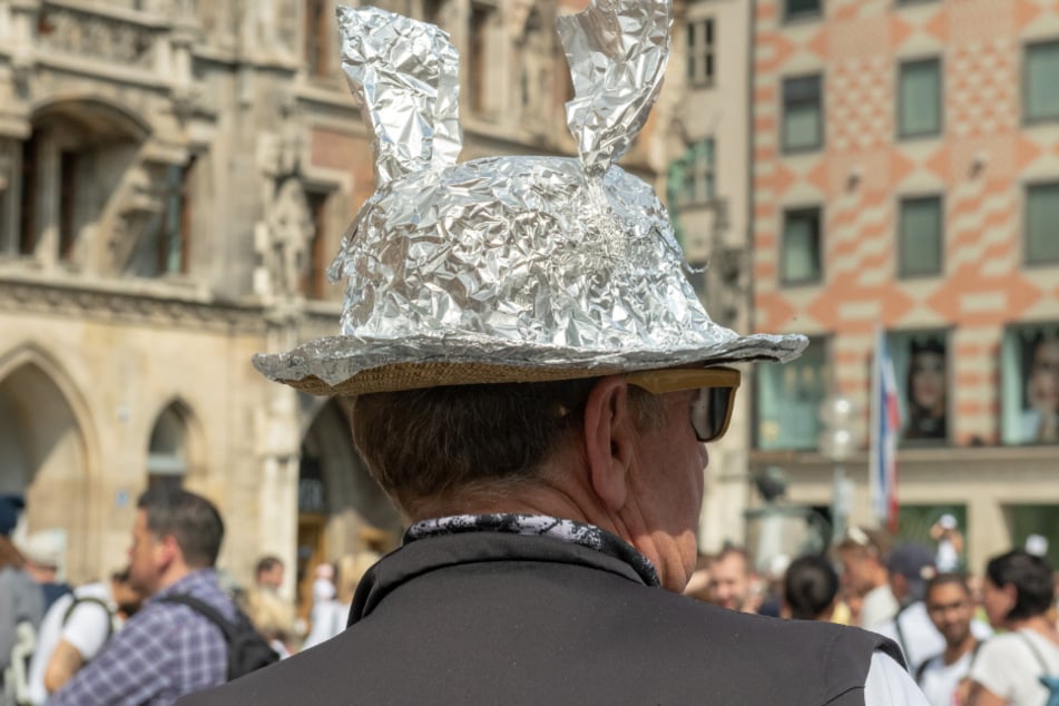 Ein Demonstranten mit einem Strohhut der mit Aluminium bespannt ist, steht in einer Menschenansammlung auf dem Marienplatz. (Symbolbild)