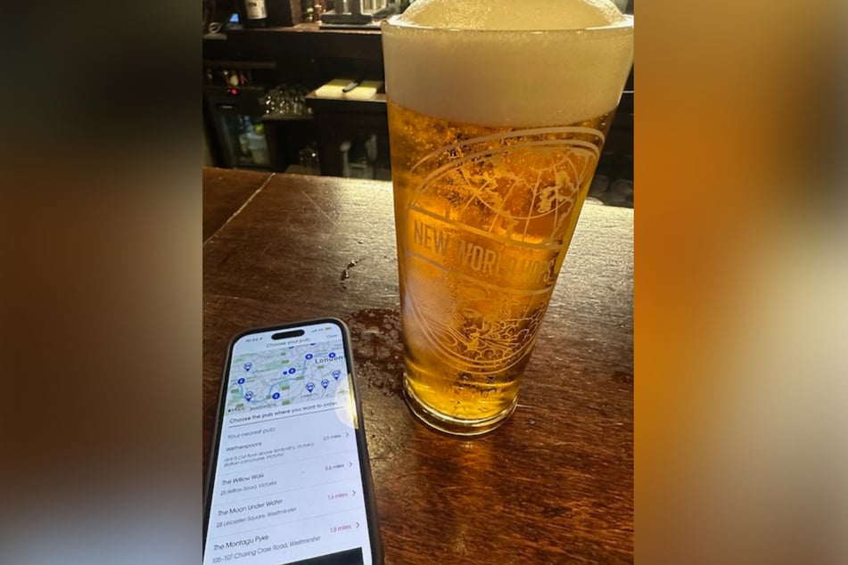 Auf einem Handy ist neben einem Pint Bier die App der Pub-Kette Wetherspoon zu sehen.