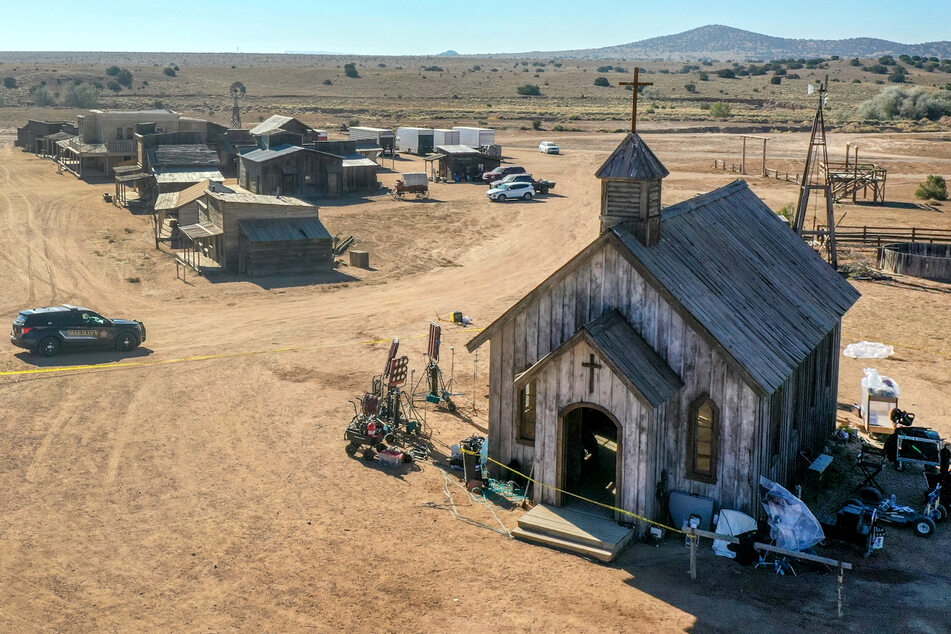 Ein Polizeifahrzeug fährt auf der Bonanza Creek Ranch an einem Gebäude vorbei, das von einem gelben Polizeiabsperrungsband umgeben ist.