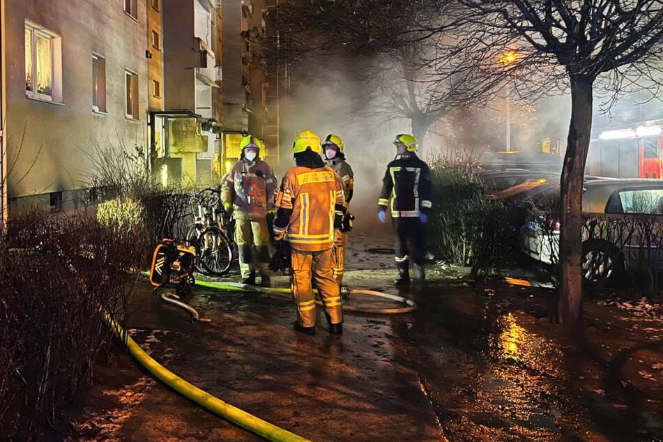 Feuerwehrleute stehen in der Nacht zum Samstag am Einsatzort in Berlin-Hellersdorf. Aus dem Kellerraum eines Wohnhauses in der Riesaer Straße dringen Rauchschwaden.