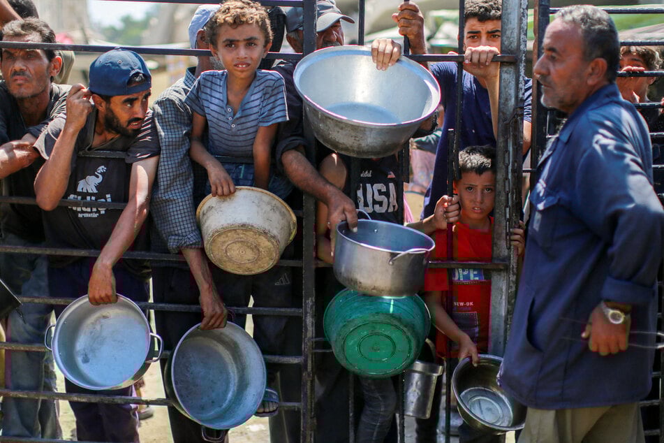 Palestinians wait as they try to get rice from a charity kitchen in the west of Gaza City on August 28, 2025.