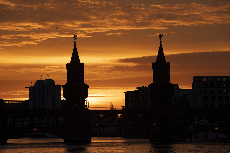 Hinter der Oberbaumbrücke in Berlin, die die Bezirke Kreuzberg und Friedrichshain verbindet, geht die Sonne auf.