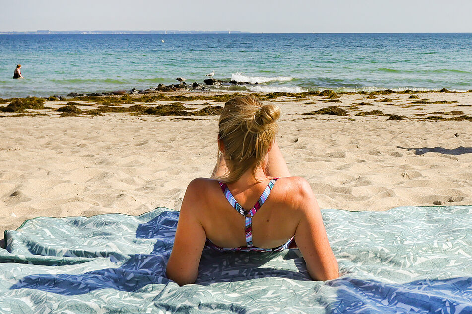 Eine Urlauberin genießt das sommerliche Wetter am Ostseeufer in Timmendorfer Strand. Der weltgrößte Reisekonzern Tui rechnet nach einem weiteren Verlustquartal mit einem schwächeren Sommergeschäft als bislang.