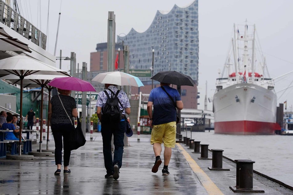 Touristen laufen mit Regenschirmen in der Hand an der Elbpromenade entlang. Im Norden Deutschlands ist es zurzeit sehr regnerisch.