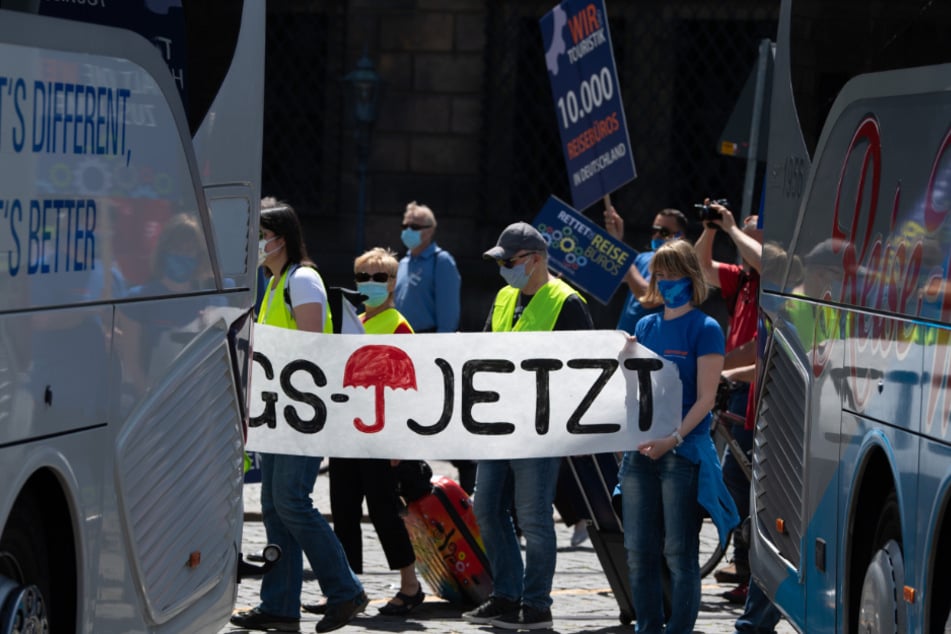 Teilnehmer einer Demonstration unter dem Motto "Touristik kurz vor der Ohnmacht" gehen auf dem Theaterplatz zwischen Reisebussen entlang.