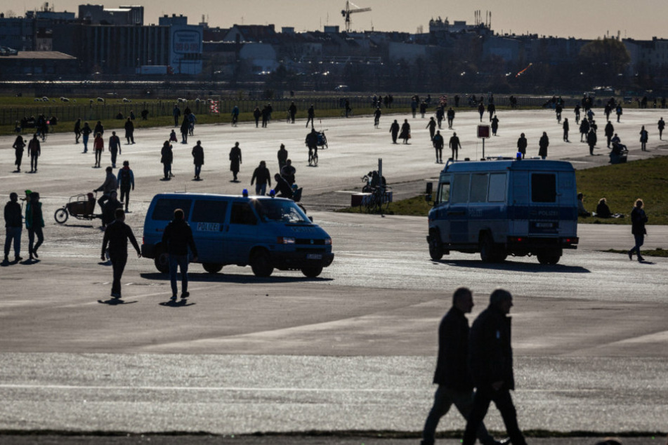 Polizeiwagen fahren zwischen Spaziergängern auf dem Tempelhofer Feld.