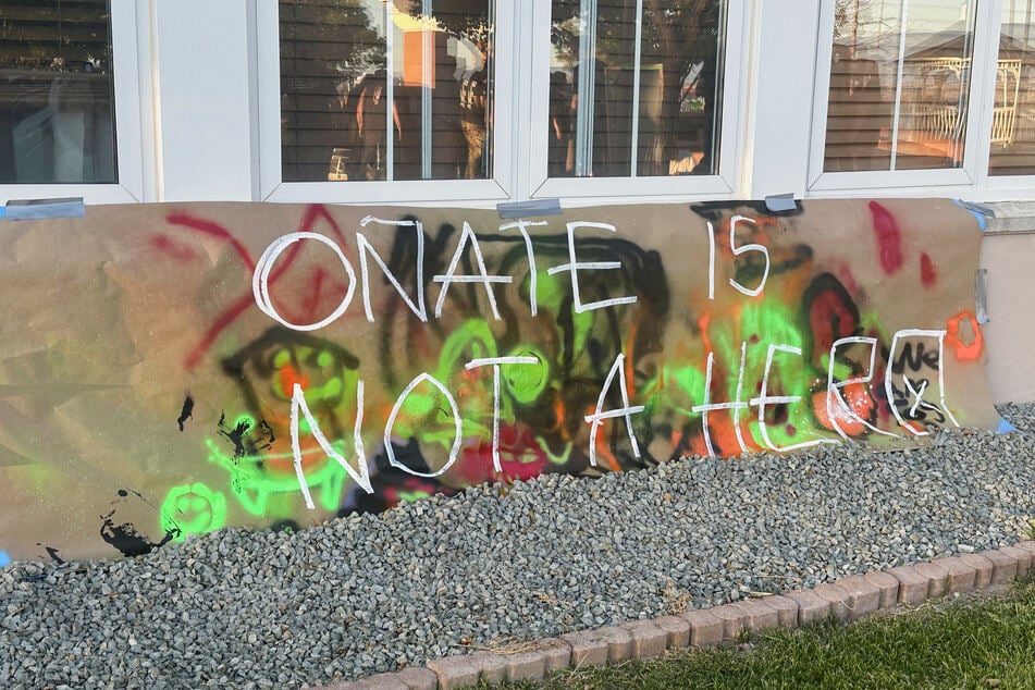 Protesters are reflected on a window as they stand next to a concrete platform where authorities had planned to reinstall a statue of Spanish conquistador Juan de Oñate at the Rio Arriba County Complex in Española, New Mexico.