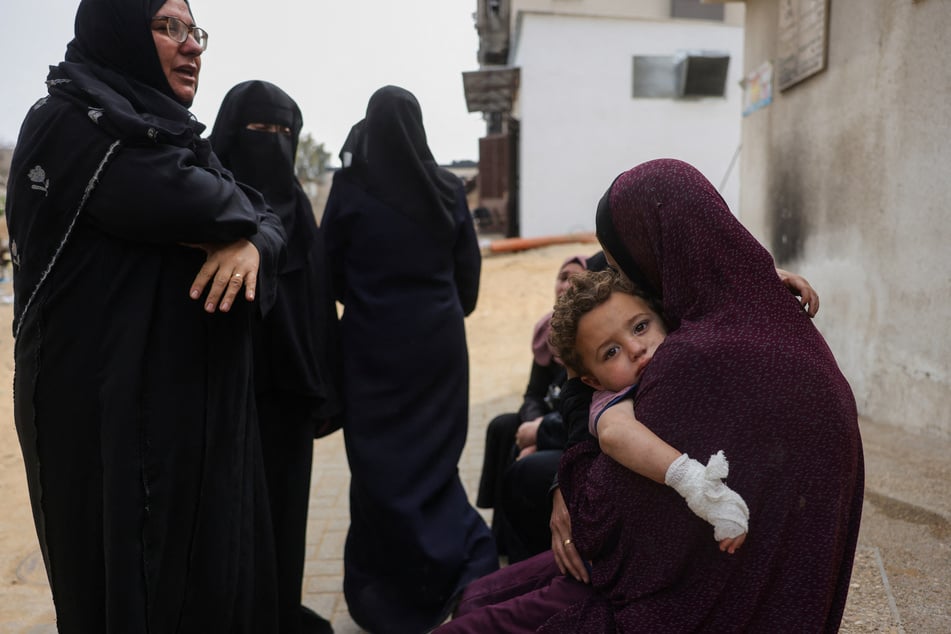 A Palestinian woman carries an injured child while sitting with others outside Al-Shifa hospital in Gaza City on May 18, 2025.