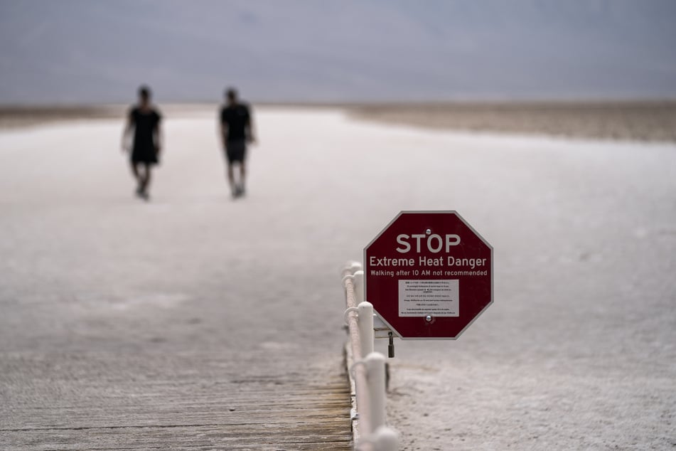 Ein Schild warnt vor extremer Hitze, während Menschen auf den Salzflächen im Badwater Basin spazieren gehen, im Death Valley National Park, Kalifornien.