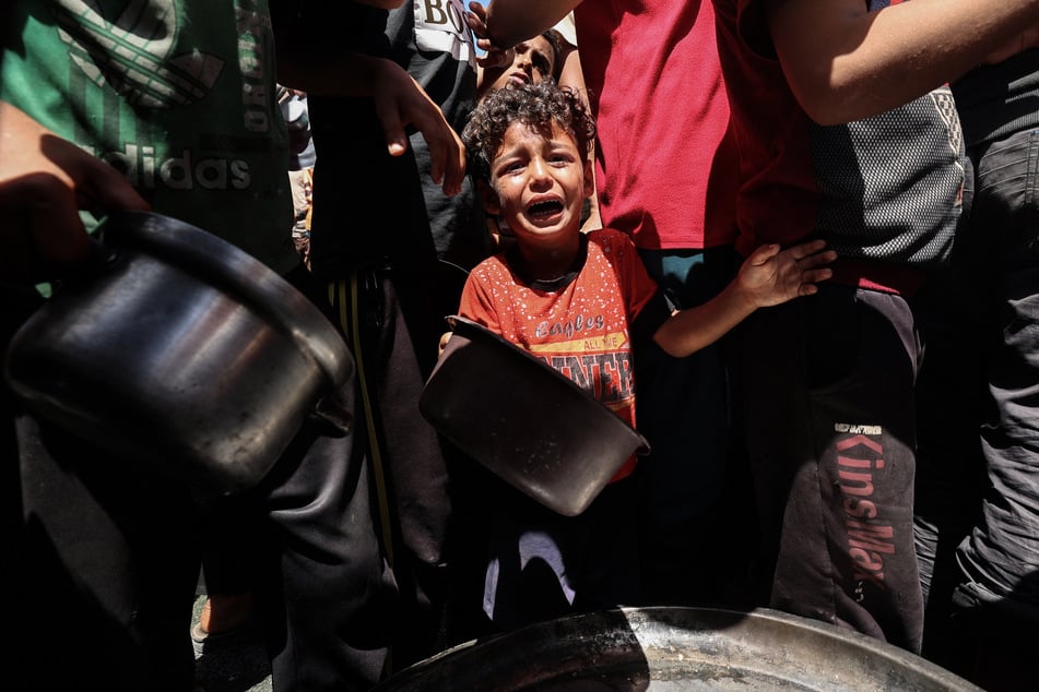 A child cries as Palestinians gather to receive a hot meal at a food distribution point in the Nuseirat camp for refugees in the central Gaza Strip on May 24, 2025.