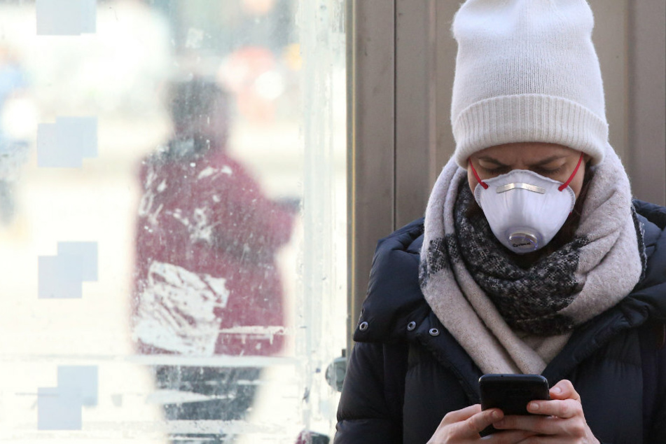 Eine junge Frau mit Schutzmaske informiert sich auf dem Alexanderplatz im Bezirk Mitte mit ihrem Smartphone über die Nachrichtenlage und über die weitere Entwicklung beim Coronavirus.