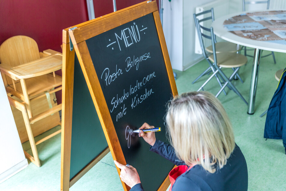 Jana Messerschmidt schreibt das Menü des Tages an die Tafel: Pasta Bolognese und eine Schokocreme als Nachtisch.