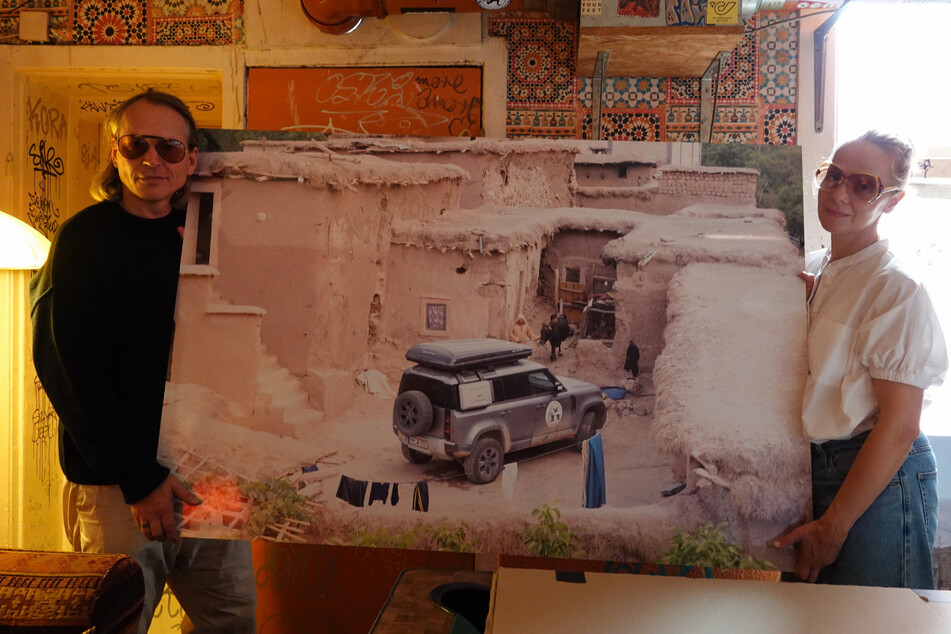 Die beiden halten eines ihrer Fotos von Häusern eines marokkanischen Dorfes, die inzwischen teilweise zerstört sind.