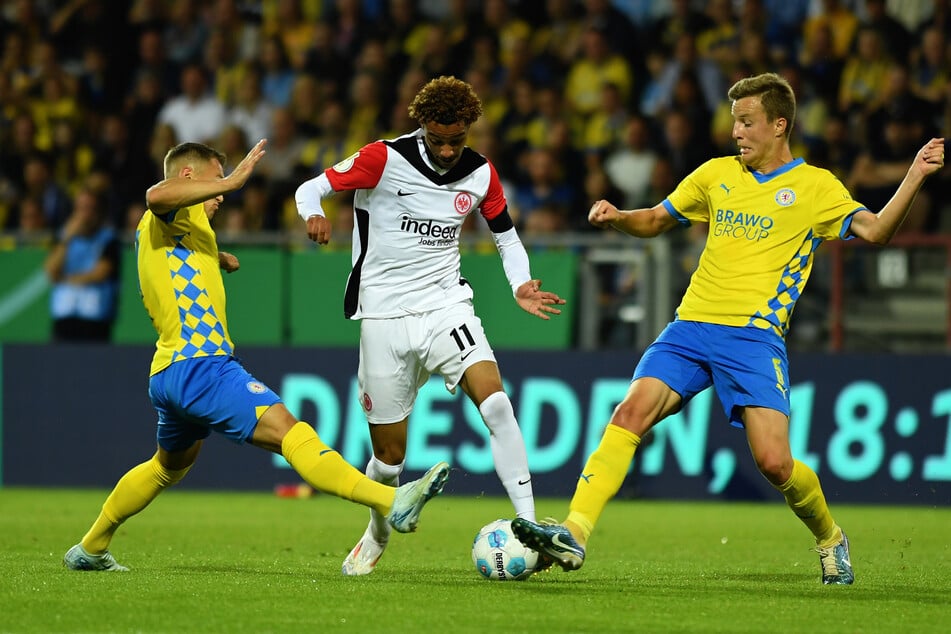 Frankfurts Hugo Ekitike (Mitte) behauptet sich am Ball gegen die beiden Braunschweig-Akteure Obert Ivanov und Sven Köhler.