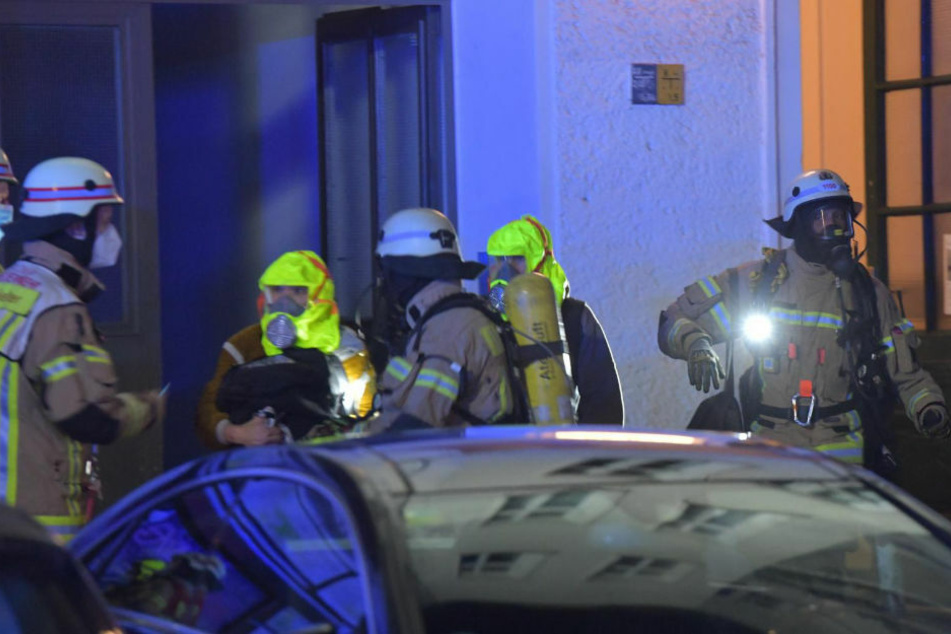 Die Feuerwehrleute bringen zwei gerettete Personen mit Fluchthauben aus dem Haus heraus.