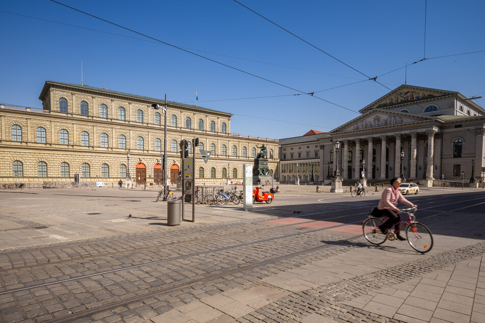Eine Radfahrerin fährt über den fast menschenleeren Max-Joseph-Platz; links der Königsbau und rechts die Bayerische Staatsoper.