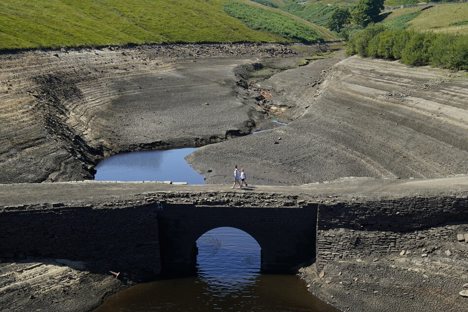 Zwei Personen gehen auf einer Brücke über das Baitings Reservoir bei Ripponden, wo der Wasserstand deutlich niedrig ist.