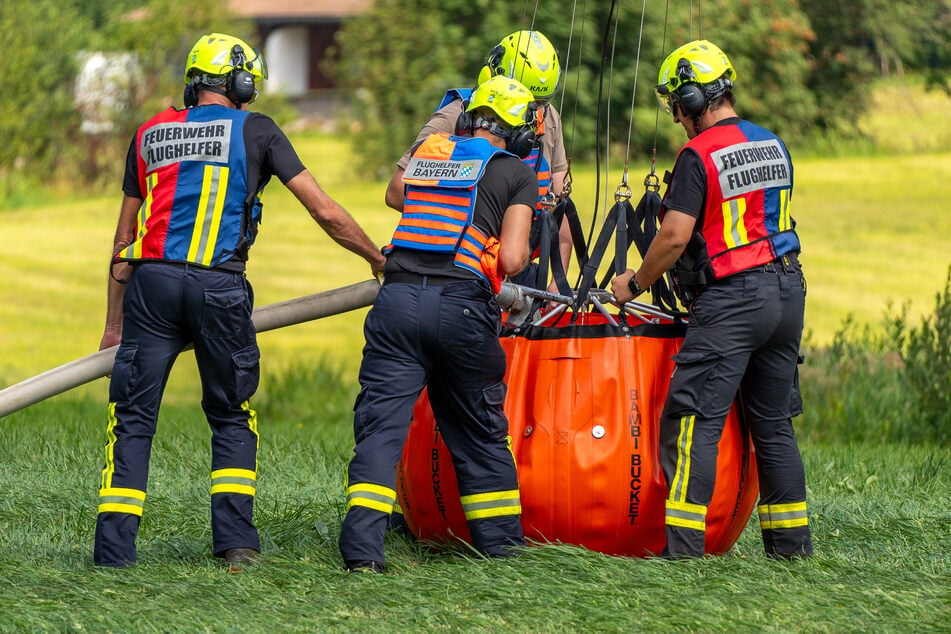 Einsatzkräfte befüllen ein Behältnis mit Wasser, sodass es vom Hubschrauber ins Brandgebiet geflogen werden kann.