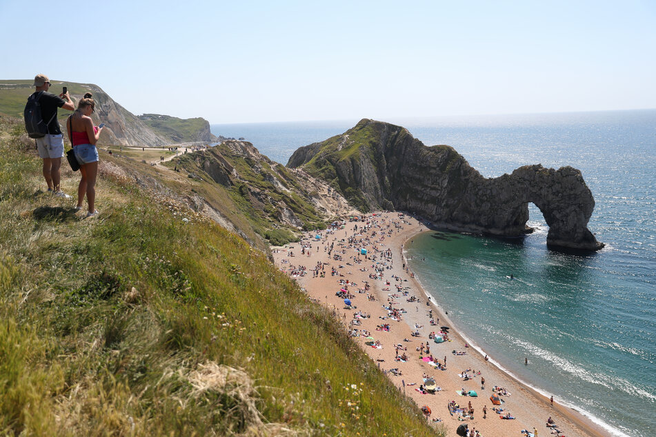 Zahlreiche Menschen halten sich am Strand bei Durdle Door, einer natürlichen Felsbrücke aus Kalkstein, auf, obwohl der Gemeinderat von Dorset den Strand für die Öffentlichkeit geschlossen hat, nachdem sich drei Menschen bei Sprüngen von den Felsen schwer verletzt hatten.