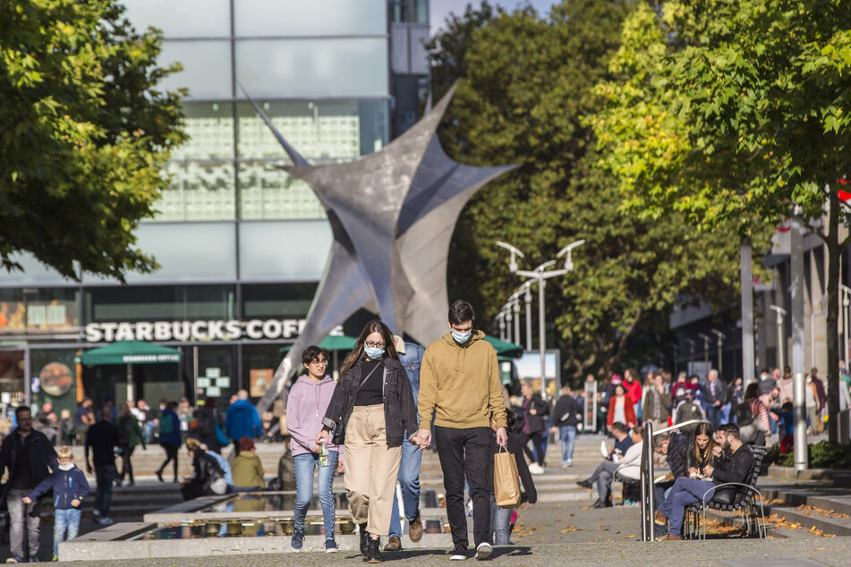 Personen gehen mit Mundschutz über die Prager Straße in Dresden.