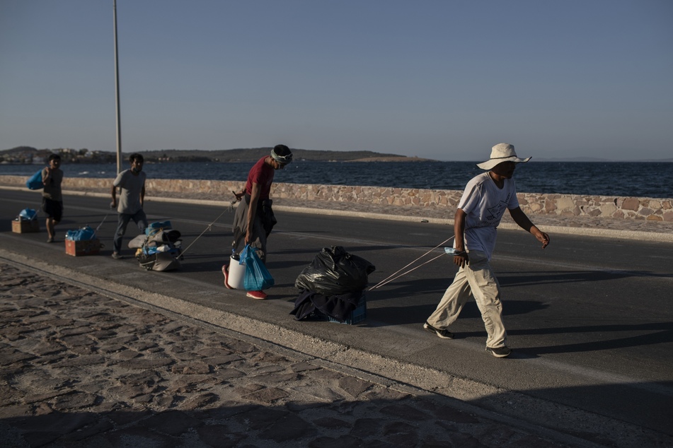 Migranten ziehen ihre Habseligkeiten mit sich und gehen entlang einer Straße in der Nähe der Stadt Mytilene auf der nordöstlichen Seite der Insel Lesbos.