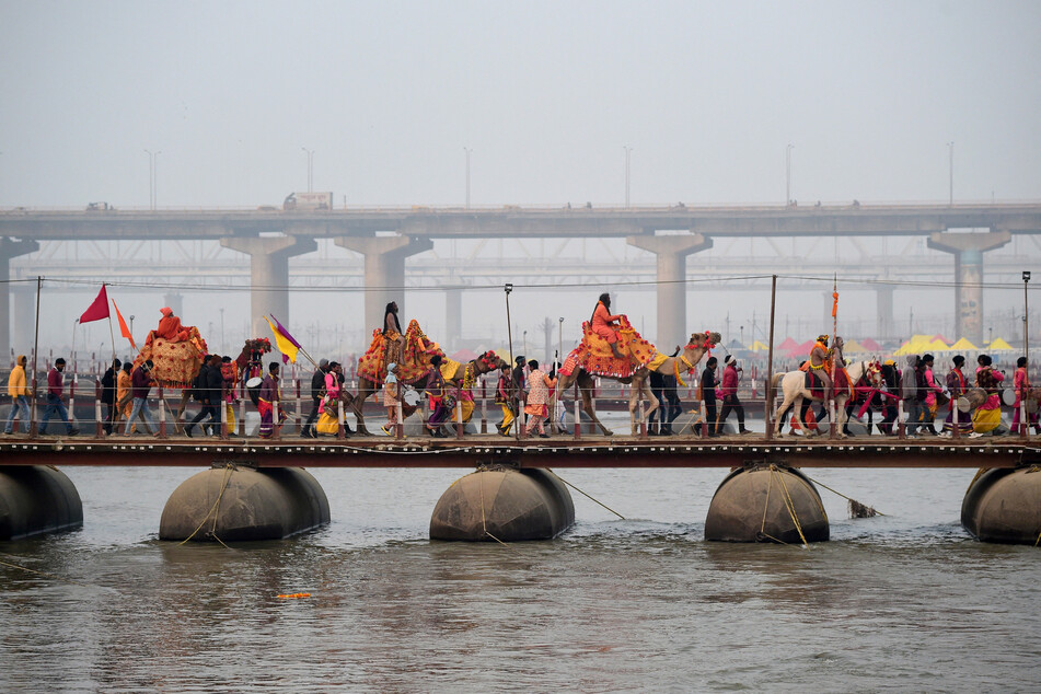 Naga Sadhus and devotees cross a pontoon bridge spanning the river Ganga as they take part in a religious procession during Peshwai in Prayagraj, India.