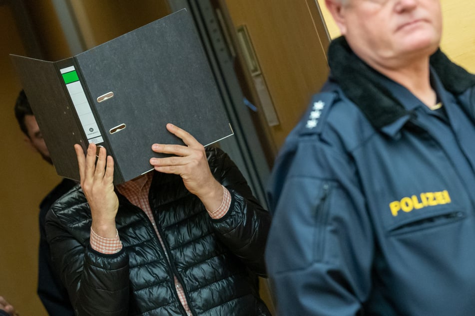 Der wegen Missbrauchs von Kindern angeklagte Logopäde trifft zum Prozessbeginn im Sitzungssaal im Landgericht ein und hält sich einen Aktenordner vor das Gesicht.