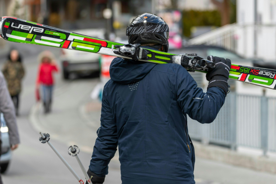 Ein Skifahrer geht mit geschulterten Skiern auf einer Straße.