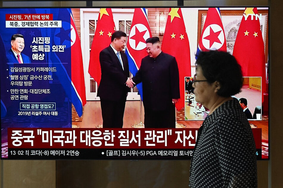 A woman walks past a television screen showing a news broadcast with file footage of the 2019 meeting between China's President Xi Jinping and North Korean leader Kim Jong Un, at a train station in Seoul on June 8, 2026.