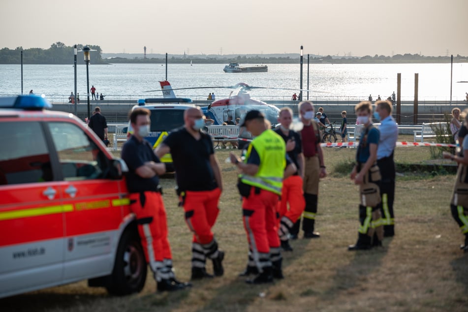 Einsatzkräfte der Feuerwehr und ein Helikopter stehen am Willkommhöft an der Elbe.