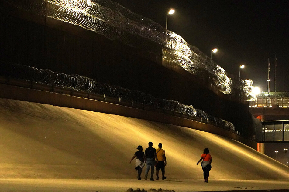Migrants walk by the US Border Wall after crossing Rio Bravo from Mexico to the US.