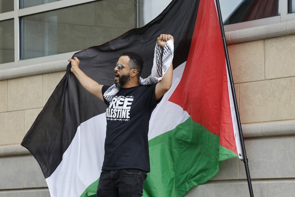 A demonstrator holds a keffiyeh and stands in front of a Palestinian flag during a protest outside the Arab American National Museum in Dearborn, Michigan.