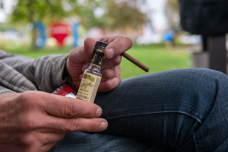 Ein Mann sitzt mit einer kleinen Flasche Schnaps auf dem Thomas-Mann-Platz.