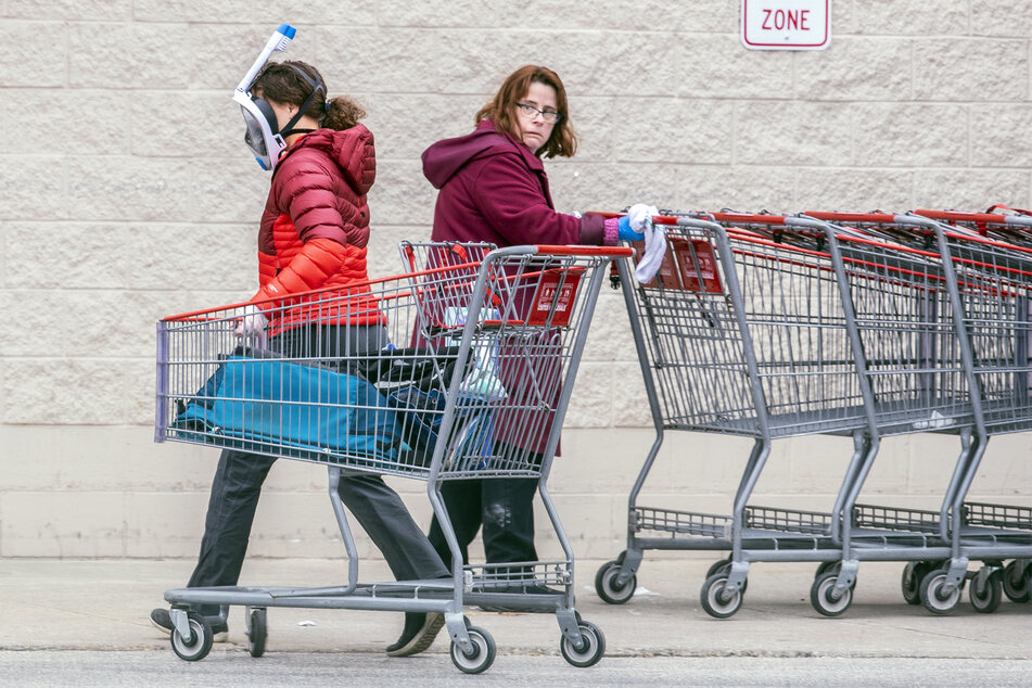 Eine Mitarbeiterin eines Supermarkts Costco desinfiziert Einkaufswagen, während sie auf eine Kundin reagiert, die eine Schnorchelmaske trägt.