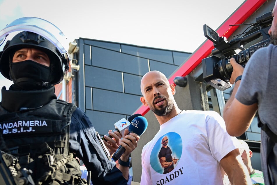 Andrew Tate (c.) speaks to journalists as he is brought in for questioning by the Romanian gendarmes after a ten-hour-long raid by police at his residence in Bucharest on August 21, 2024.