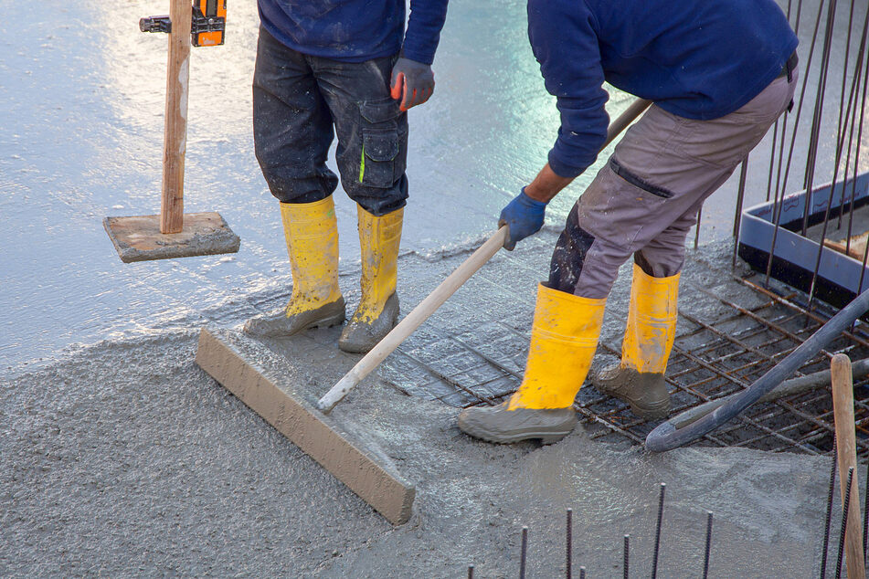 Two workers spread concrete for a floor slab with ready-mixed concrete.